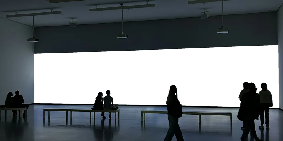 Große LED-Wand in einer Halle, davor bleiben Besucher stehen. Auf der Wand läuft ein Film von Explikate.